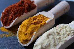 white wooden big three spoons are filled with organic Indian spices red chili powder, turmeric powder, coriander powder with background of navy color