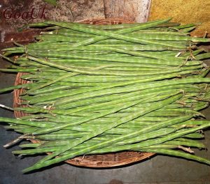 a basket filled with green drumstick beans sitting on top of the floor.